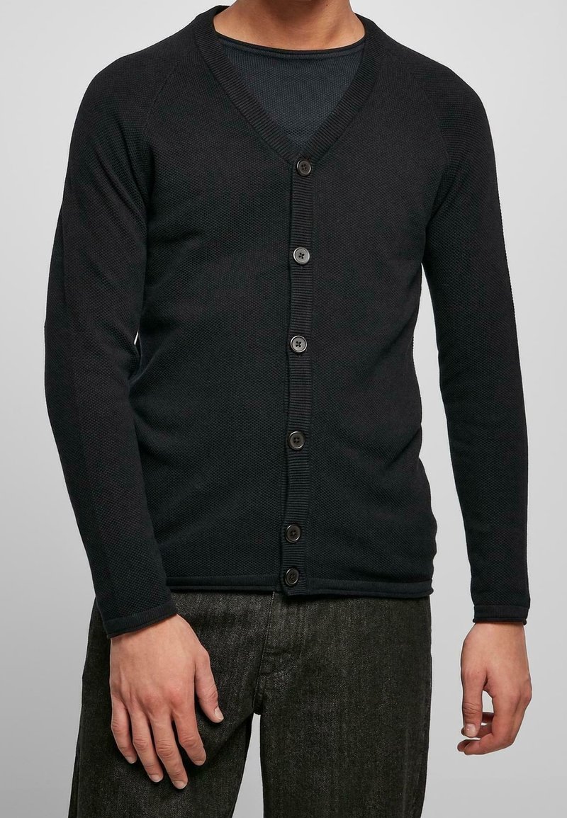 Svart stickad cardigan med V-ringning, knappstängning och strukturerad tyg. Har långa ärmar och en figurnära design.