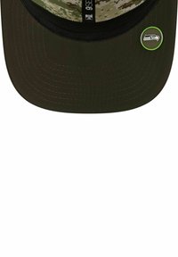 Dunkelgrüne Mütze mit einem strukturierten Frontteil, camouflierte Innenseite, flacher Spitze und einem grünen Logoakzent an der Seite mit einem Vogelwappen.
