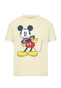 Light beige t-shirt featuring a graphic of a cartoon mouse with black ears, red shorts, and yellow shoes, smiling with hands on hips.