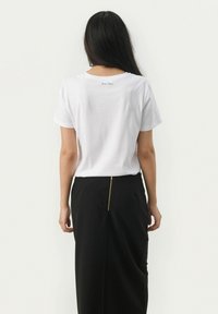 T-shirt bianco in cotone con scollo rotondo, con la scritta "Part Two" stampata vicino alla parte superiore della schiena; abbinato a una gonna nera con una zip dorata.