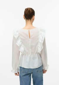 Blusa bianca con maniche arricciate, dotata di una schiena a chiave e vita cinquecent. Il tessuto è leggero con una sottile texture a righe. Stile casual.