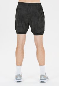Svarta idrottsshorts med ett kamouflage-mönster, elastisk midja och inbyggda svarta kompressionsshorts. Bärs med grå löparskor.