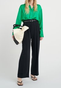 Camicia verde satinata con bottoni, pantaloni neri a vita alta e una borsa bicolore con tracolle nere. Sandali neri con fasce completano il look.