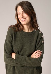 Pull en maille vert olive avec un col rond, des manches longues et des accents de boutons sur l'épaule. Tissu texturé avec une apparence confortable.