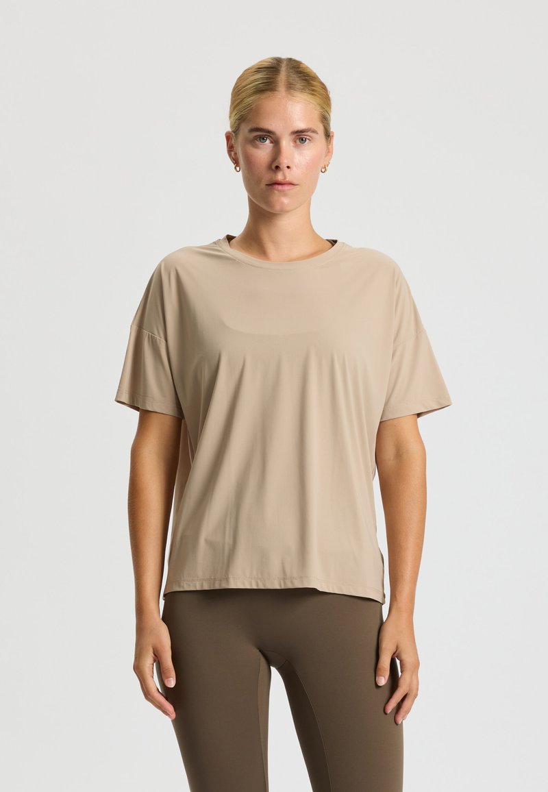 T-shirt beige à manches courtes en tissu léger et lisse. Coupe décontractée avec un col rond, associé à des leggings marron ajustés.