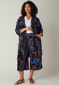 Svart tygoutfit med djärva blå och orange blommönster. Inkluderar en löst sittande sjal och vida byxor, kompletterat med en vit topp.