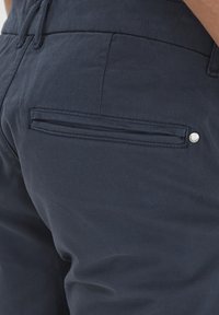 Pantaloni bleumarin dintr-un material texturat, cu un buzunar vertical pe spate dotat cu un detaliu din metal și talie elastică.