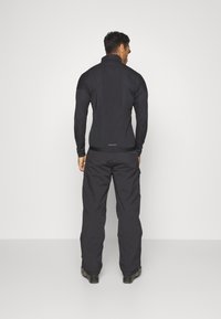 Black fleece jacket with a high collar and fitted design, paired with black pants. The outfit features a smooth texture and streamlined shape.