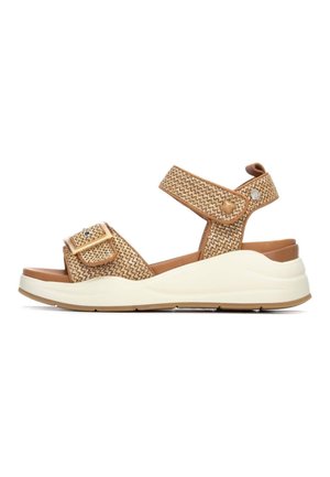 Sandalias tejidas de color canela con correas ajustables, punta redondeada y suela gruesa blanca. Presentan una hebilla decorativa y una superficie texturizada.