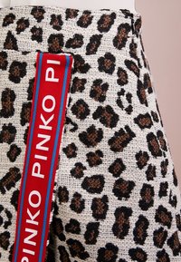 Látka s leopardím vzorem v béžové, černé a hnědé barvě, s červeným pruhem s textem "PINKO" a modrými akcenty po straně.