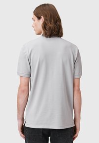 Grijs polo-shirt met korte mouwen en een gladde textuur, met een rechte onderrand en zijsplitten, weergegeven vanuit de achterkant.