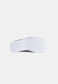Sula på en sko med en texturerad vit gummimaterial, med ett mönstrat ytskikt, böjd form och lätt svank för komfort.