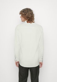 Camicia a maniche lunghe beige chiaro con colletto a bottoni, caratterizzata da un orlo dritto e polsini con chiusura a bottone. Tessuto dalla trama liscia.