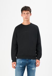 Black sweatshirt with a crew neckline, ribbed cuffs, and hem. Features embossed "REPLAY" logo on the front. Paired with distressed blue jeans.