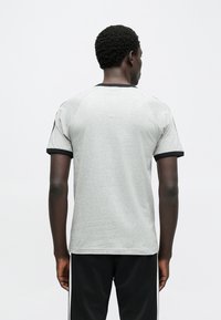 Γκρι κοντομάνικη μπλούζα με μαύρο γιακά και μανίκια· διαθέτει ραγκλάν κοπή και λεία υφή, εμφανιζόμενη από την πίσω πλευρά.