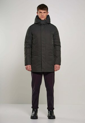 Parka isolante grigio scuro con cappuccio, zip frontale e tasche laterali. Indossato sopra pantaloni scuri e stivali neri alla caviglia. Tessuto liscio.