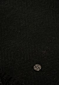 Tessuto nero testurizzato con motivo a spina di pesce, caratterizzato da un piccolo logo metallico nell'angolo inferiore. Aspetto morbido e caldo.