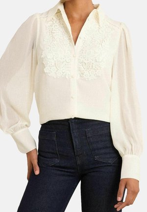 Witte blouse met lange mouwen en kantdetail op de borst, knoopsluiting aan de voorkant, pofmouwen, gedragen met donkerblauwe high-waist jeans met voorzakken.