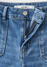 Jeans di denim blu chiaro con chiusura a bottoni e cerniera. Include cuciture visibili e un'etichetta "un giorno" nella vita.