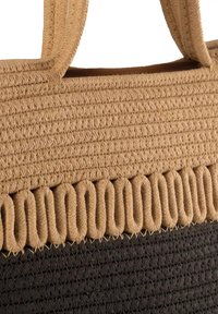 Spleciona torba z trawy z tanowymi i czarnymi sekcjami. Charakteryzuje się teksturowanym splotem oraz falbaniastym tanowym akcentem wzdłuż górnej krawędzi.
