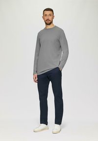 Graues langärmeliges Shirt, marineblaue Hose und weiße Sneakers. Das Outfit hat einen klassischen Rundhalsausschnitt und eine lockere Passform.