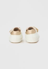 Λευκά παπούτσια με λεία συνθετική επιφάνεια, διακοσμημένα με χρυσή επιφάνεια στη φτέρνα και μπεζ λουράκι με βέλκρο. Στρογγυλερή μύτη και επίπεδη σόλα.