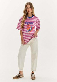 Růžové a bílé pruhované oversized tričko s barevným motivem kuřete, doplněné béžovými kalhotami a teniskami s leopardím potiskem.