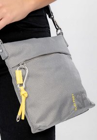 Borsa a spalla grigia in tessuto con tasca anteriore con zip, accessori in argento e una tracolla con accento giallo. La texture è leggermente decorata.
