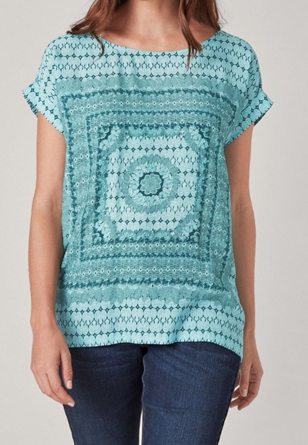 Haut turquoise à manches courtes avec un imprimé géométrique composé de motifs circulaires et carrés, tissu texturé et coupe ample.