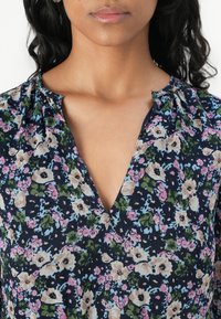 Bluză florală în nuanță de navy, cu decolteu în V, umeri gathered și un mix de modele florale în nuanțe de roz și verde. Fabricată dintr-un material ușor.