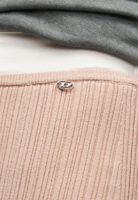 Ροζ ριγωτό ύφασμα με μικρό ασημένιο οβάλ έμβλημα, στρωμένο κάτω από γκρι και λευκά υφάσματα ρούχων.