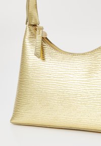 Gold, textured shoulder bag with a curved shape, featuring a zip closure and an adjustable strap. The surface has a wavy pattern.