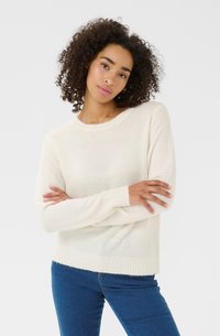 Pull beige à col rond, à manches longues et avec des bords ribbés. Texture douce, associé à un jean bleu.
