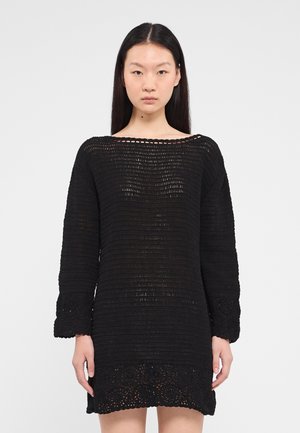 Black knit dress with long sleeves, featuring a ribbed texture and lace hem detail. Relaxed fit with wide neckline, showcasing open weave.
