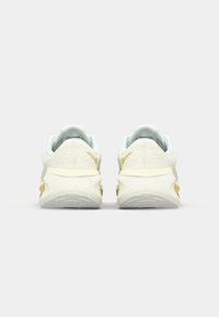 Lichtgekleurde sportschoenen met een gestructureerde bovenkant, een gevoerde kraag, gele accenten en een contrasterende witte zool.