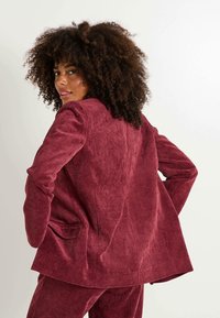 Blazer de pana burdeos con rayas verticales, dos bolsillos laterales y un corte relajado. Textura suave con una silueta ligeramente holgada.