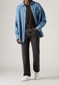 Camisa de mezclilla en azul claro con diseño de botones, camiseta negra, jeans negros y zapatillas blancas. Corte relajado con un estilo sencillo.