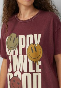 Bordeaux, oversize T-shirt wykonany z miękkiego materiału, z trzema kolorowymi, skapującymi buźkami oraz dużym, wyraźnym białym napisem.