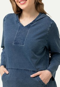 Modrá mikina s kapucí, výstřihem do V, přední kapsou a dlouhými rukávy, s měkkou texturou a uvolněným designem.
