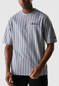 T-shirt en coton gris avec des rayures verticales noires, col rond, manches courtes et logo "New Era" discret en noir sur la poitrine.