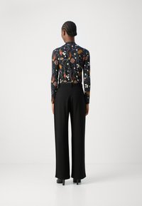 Dlouhý rukáv má černý základ s barevným květinovým vzorem. Široké černé kalhoty doplňují outfit. Hladká látka s přiléhavým střihem.