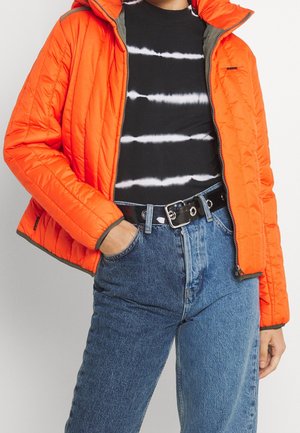 Osoba ubrana w pomarańczową pikowaną kurtkę, czarno-białą koszulę w paski, niebieskie dżinsy wysokiej talii i czarny pasek ze srebrną klamrą.