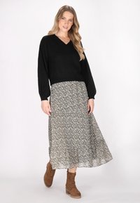 Schwarzer V-Ausschnitt-Pullover, gemusterter langer Rock mit kleinen weißen Blumen auf dunklem Hintergrund und braunen schnürbaren knöchelhohen Stiefeln.