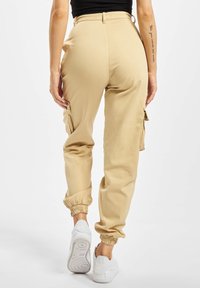 Beige cargopants met een elastische tailleband en boorden, met zijzakken. G gedragen met witte sneakers voor een casual uitstraling.