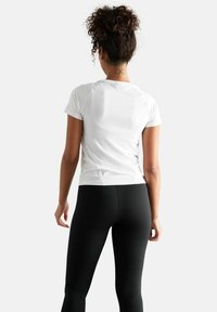 Witte T-shirt met korte mouwen en een aansluitend design, gedragen met zwarte leggings. Het T-shirt heeft een gebogen zoom en een lichtgewicht stof.