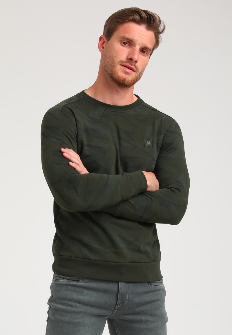 Zelená camouflage mikina s dlouhými rukávy, kulatým výstřihem a žebrovanými manžetami. Měkká látka s jemným vzorem a malým logem.
