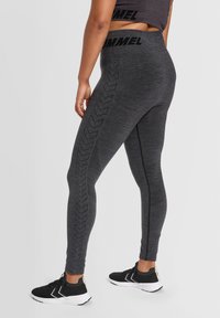 Grå idrottstights med en texturerad yta, med ett horisontellt band i midjan och ett zigzag-mönster längs den yttre benet.