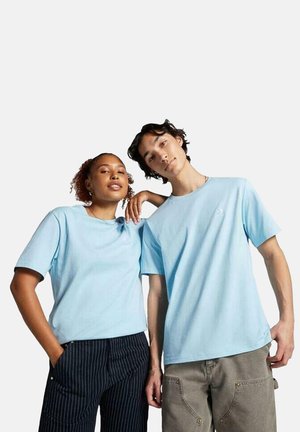 Dos personas llevan camisetas de algodón de color azul claro a juego, con mangas cortas y cuellos redondos. Las camisetas tienen un diseño minimalista.
