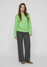 Svetlo zelena jopica s okroglim izrezom, rebrastimi manžetami in robom; v kombinaciji s širokimi temno sivimi kavbojkami in svetlo rjavim footware-om.