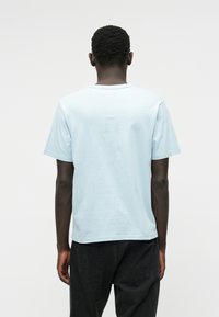 Camiseta de algodón de color azul claro con mangas cortas y cuello redondo, vista desde la parte de atrás. Combinada con unos jeans oscuros, diseño minimalista.